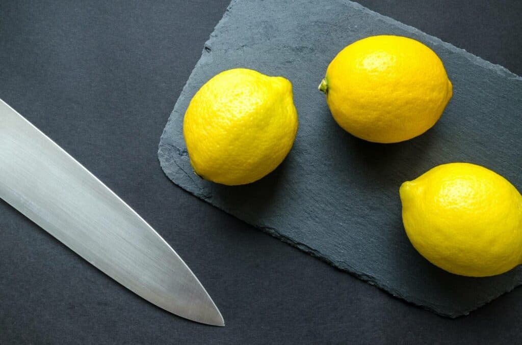Three lemons on a stone cutting board next to a knife